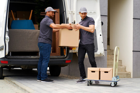 Man helping colleague while unloading boxes from van