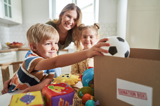 Smiling boy putting toy in donation box with family in background at home