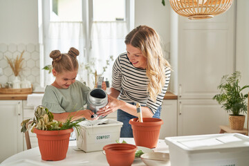 Mother and daughter watering homemade compost in container on table