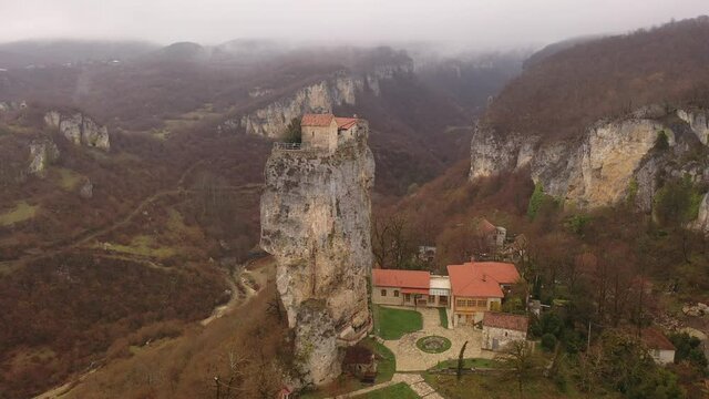 Aerial view of small church of St. Maximus Confessor with red tiled roof on top of narrow high limestone Katskhi pillar in mountainous region of Georgia