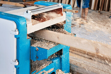 A wood plate passing through the thickness planer machine in a carpentry workshop.
