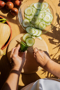 Woman cutting cucumber with knife at kitchen