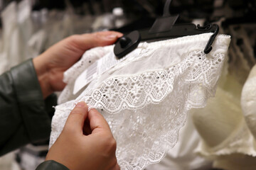 Woman chooses white lace panties in lingerie store, selective focus on hands. Female fashion, different sizes of wedding underwear