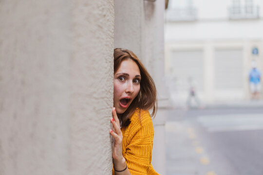 Surprised woman with brown hair peeking from wall