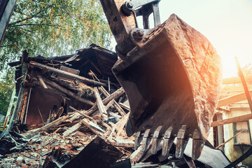 Fototapeta premium Demolition building construction concept. Excavator shovel or bucket at background of debris broken house.