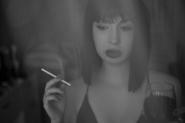 Fototapeta premium Young beautiful woman in a black wig, like Cleoparta with glass of wine and cigarette, a little pensive and sad. Black and white photography. Close up portrait. Soft photography.