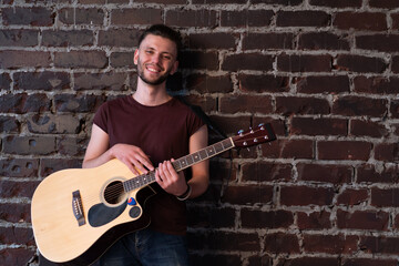 Man with acoustic guitar against brick wall playing music singing songs enjoy life Medium shoot