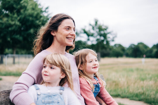 Smiling mother sitting with daughters at public park