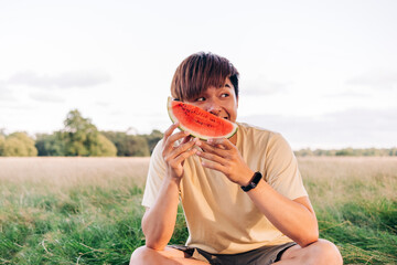 Young man holding watermelon slice while sitting on meadow