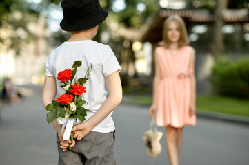 Fototapeta premium Children's date, boy hides flowers from a girl