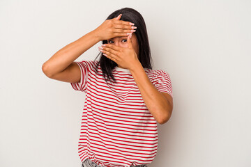 Young latin woman isolated on white background  blink at the camera through fingers, embarrassed covering face.