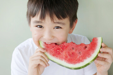 Happy cute asian child boy eating red watermealon indoors