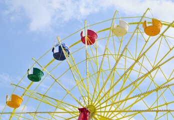 Ferris wheel with multicolored cabins without passengers against blue sky in the park
