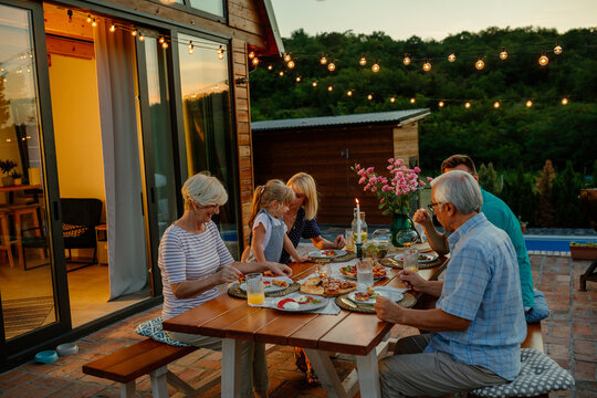 Multi-generation family having dinner outdoors in the backyard - Powered by Adobe