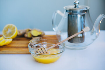honey in a glass cup, teapot, lemon and ginger on a white background. Preparing a cold drink