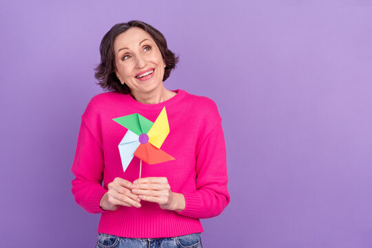 Portrait of attractive cheery dreamy mature woman holding paper fan playing isolated over violet purple color background