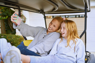 Happy girls taking selfie while sitting in golf cart
