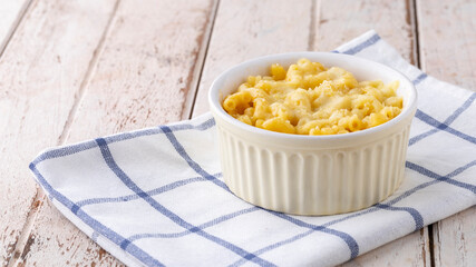 Mac and Cheese, macaroni pasta with cheese in ceramic bowl on napkin on white old wood texture background