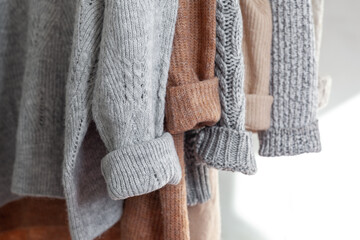 Pastel warm knitted clothes sweater hanging in the closet. Cozy autumn and winter wardrobe. - obrazy, fototapety, plakaty