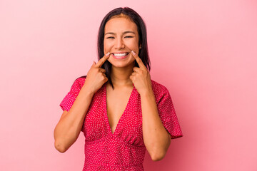 Young latin woman isolated on pink background  smiles, pointing fingers at mouth.
