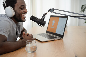 African man recording a podcast using microphone and laptop from his home studio - obrazy, fototapety, plakaty