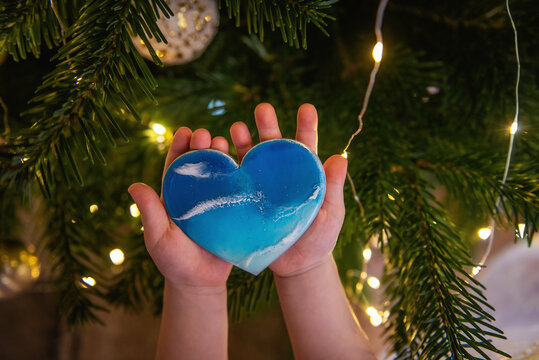 Childrens hands hold in the palms Christmas toy in the form of heart with the image of the sea coast