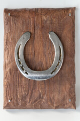 A shiny metal horseshoe, nailed with forged nails to a painted matte board. A souvenir for storing keys. On a light background.