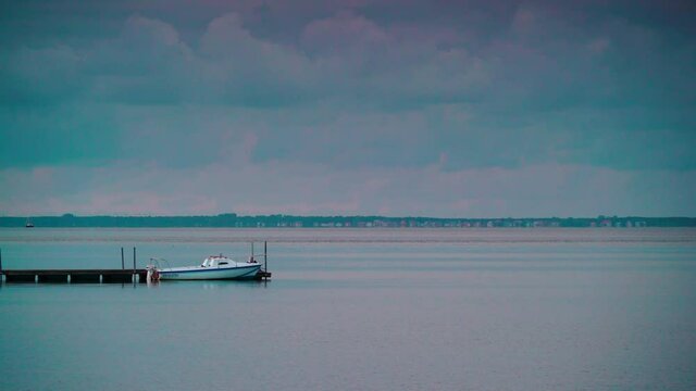 Seascape at evening with boat tied to wooden pier. Baltic Sea, Puck Bay in Poland with Hel Peninsula on horizon. Seaside coast landscape.