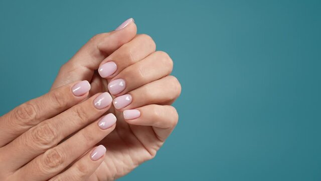 Close-up top view 4k stock video footage of elegant minimal pastel pink natural manicure. Female hands isolated on blue background. Naildesign with cute white hearts to Valentine's day holiday