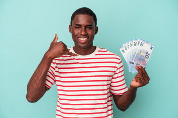 Young African American man holding a bank notes isolated on blue background showing a mobile phone call gesture with fingers.