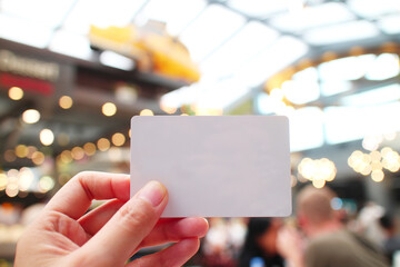 A hand holding a blank card with blur background of public space