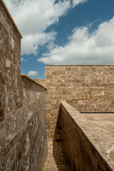 Architectural composition of walls covered in brown marble with down stairs and blue sky with clouds