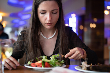 Young vegetarian woman eating salad in restaurant