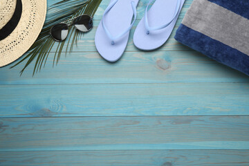 Beach towel, straw hat, flip flops and sunglasses on light blue wooden background, flat lay. Space for text