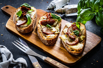 Tasty sandwiches - baked bread with camembert, basil pesto and sun dried tomatoes on wooden table
