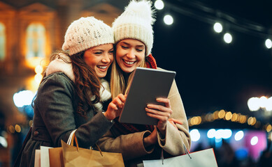 Happy women friends using digital tablet for online shopping at Christmas in the city.