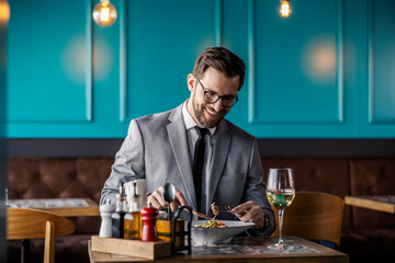 A businessman having lunch at a restaurant. A man elegantly dressed in a business suit eats pasta and drinks white wine alone in a restaurant. Lunch break between two business meetings, enjoying meal