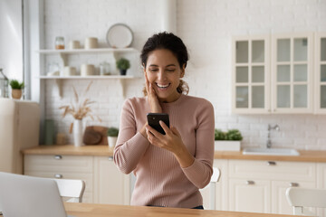 Overjoyed millennial female look at cellphone screen triumph win online lottery on gadget. Smiling excited young Caucasian woman feel euphoric read good promotion or hiring news on smartphone.