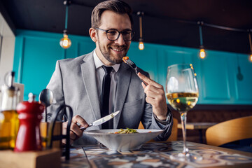 The man is about to take a bite of food, the man has lunch at a restaurant. A man elegantly dressed in a business suit eats and drinks in a restaurant. Business lifestyle, meals in restaurants