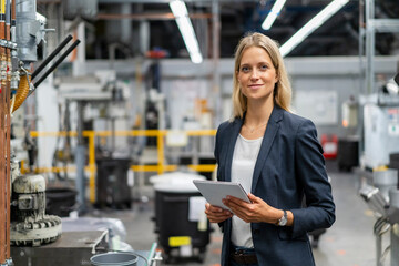 Young blond female manager holding digital tablet at industry
