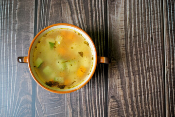 chicken broth with vegetables and zucchini in a brown plate lies on a wooden table. top view. homemade food