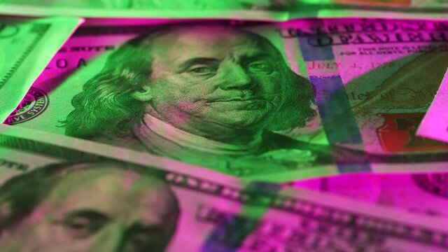 Rotating close up camera shot focused on founding father Benjamin Franklin face portrait on green and pink illuminated American dollar bill. Paper money, US banknotes. Hundreds of cash bills filmed.