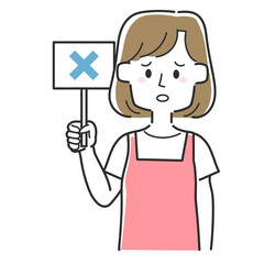 バツの書かれた札を持っているエプロンを着た主婦