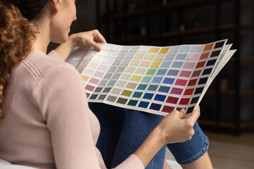 Close up back view of female renter or tenant think of house apartment renovation redecoration. Woman choose color from template or palette, renovate home living room. Interior design concept.