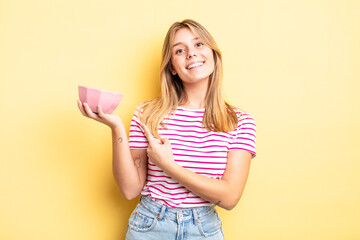 pretty blonde girl smiling cheerfully, feeling happy and pointing to the side. empty bowl concept - obrazy, fototapety, plakaty