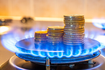 Gas stove lit, with stacks of coins above it. Increase in gas costs and tariffs.

