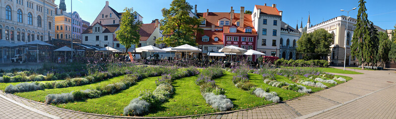 Fototapeta na wymiar Livu square in Riga, Latvia, panoramic image with wave pattern of flowerbeds on foreground. The square was once a riverbed.