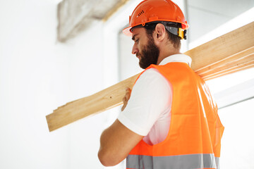 Builder man in hardhat carrying timber on building site, close up .