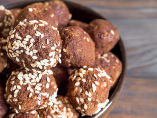 Brown.vegetarian sweets close-up, garnished with sesame seeds and carob powder in a ceramic bowl on a wooden table. Energy balls.  Raw food sweets. Proper nutrition.