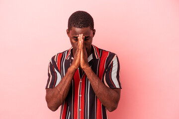 Young African American man isolated on pink background holding hands in pray near mouth, feels...
